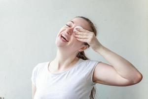 mujer sonriente con una piel suave y saludable quitando el maquillaje con una almohadilla de algodón aislada de fondo blanco foto