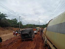 foto de carreteras de laterita dañadas que dan lugar a largas colas de vehículos muy cargados.