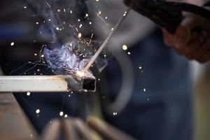 The connection of two parts by welding close-up. Metal wroker in blur in a factory grinding with sparks photo