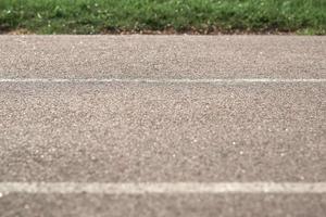 carretera pavimentada de textura con marcas en el fondo de la hierba verde. parte de la foto está borrosa.