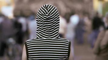 Rear view lonely girl in a vest with a hood stands against the crowd. Background in blur. photo