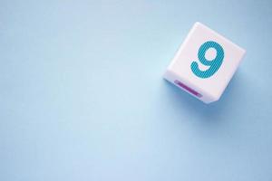 Close-up photo of a white plastic cube with a blue number 9 on a blue background in the upper right corner. With copy space