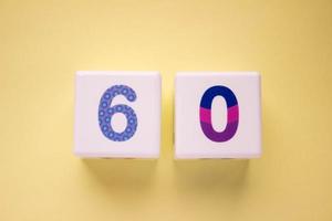 Close-up photo of a white plastic cubes with a colorful number 60 on a yellow background. Object in the center of the photo