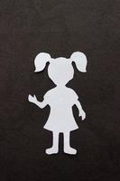 The form of a girl in a dress and with ponytails made of white paper, cut by hand. In the center of vertical photo