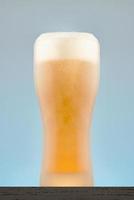 Misted glass of beer with foam. Beer glass close-up on a grey-blue background. photo