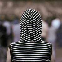 Rear view lonely girl in a vest with a hood stands at a street concert. Background in blur. photo