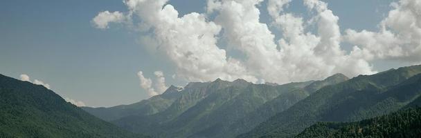 View of the green mountains illuminated by bright sunlight on the background of great white clouds. photo