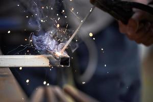 The connection of two parts by welding close-up. Metal wroker in blur in a factory grinding with sparks photo