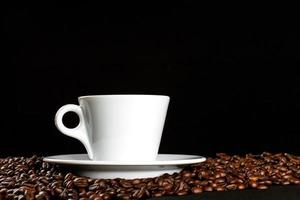 café caliente en una taza de café con leche y muchos granos de café colocados sobre un fondo oscuro, con espacio para copiar. foto