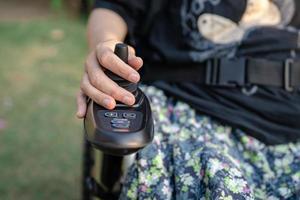 mujer asiática paciente en silla de ruedas eléctrica con joystick y control remoto en la sala del hospital de enfermería, concepto médico fuerte y saludable foto