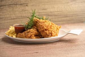 Pollo frito y papas fritas con hojas de romero, comida chatarra alta en calorías servida en un plato blanco foto