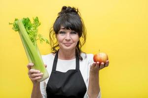 beautiful age woman cook holding an apple and celery in her hands photo