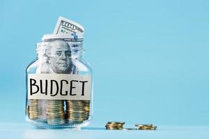 Glass jar with coins and dollars, with a sticker saying Budget, on a blue background. photo