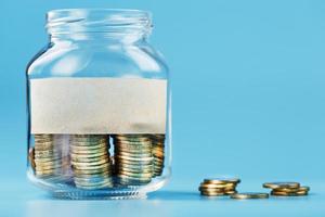 A glass jar with coins and a sticker with free space for text, on a blue background. photo