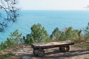 A single bench made of natural wood in the forest with a view of the sea. photo