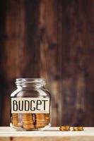 Glass jar with money and a sticker with the words BUDGET, on a wooden table. photo