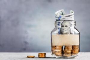 Glass Jar with gold coins, with a hundred-dollar bill and a sticker for text on a gray background with free space for text. photo