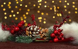 ramas de abeto con bayas rojas y piñas en un sombrero rojo de santa claus con luces de año nuevo en la parte posterior. fondo borroso tarjeta de Navidad foto
