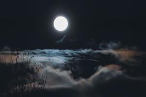 Full moon over clouds and fog in night sky, nebulous blurry landscape photo