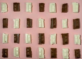 Slices of black and white chocolate on a pink background. Various chocolates on the table. photo