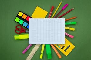 Set of stationery around a notebook on a green background. Pens, markers, felt-tip pens, scissors, calculator, paints. Back to school concept. Copy space photo