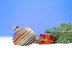 Christmas striped shiny ball with small red gift box on the snow and fir branches. New Year. Copy space photo