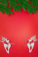 White shiny deer on red background with green branches of Christmas tree. New Year. Copy space photo