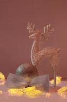 Shiny deer stands next to ball with glitter and bow and Christmas lights on pink background. New Year. Vertical. Copy space photo