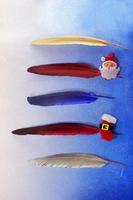 Gold, red, blue, silver feathers with pin with santa claus and a boot on a blue background. For list, write text, planning. Five lines. Christmas and New year photo