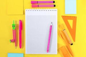 Back to school. Notebook checkered with pencil for notes for text. Nearby yellow, pink, orange stationery. Ruler, markers, felt tip pens, adhesive note, pens, compasses. Learning concept. Copy space photo