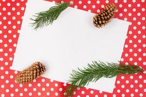 Fir twigs and cones on red background with polka dot and white sheet for text. Christmas, New Year, autumn, winter. Copy space photo