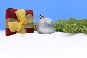 Silver glittering ball with present box in snow and green spruce branches on blue background with place for text. Christmas, New Year. Copy space photo