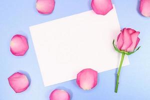 pétalos y rosa con hoja blanca de papel para texto sobre fondo azul. feriado, 8 de marzo, cumpleaños, día internacional de la mujer y la madre, st. san valentin copie el espacio foto