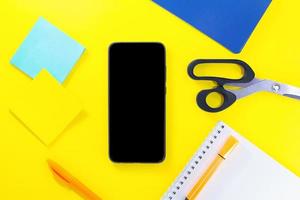 Back to school. Education flat lay. Business layout. Mobile phone mock up, notepad, pen, sticker paper, scissors on yellow background. Copy space photo