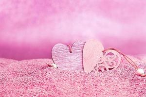 Two wooden hearts on pink sand against blurred background with bokeh. Valentine's Day. Copy space photo