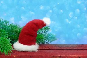 Santa Claus hat on a wooden board with fir branches on a blue background with bokeh. Christmas, new year. Copy space photo