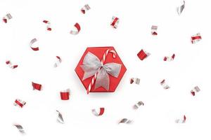 Festive red shiny gift box with silver bow and candy cane confetti isolated on white background. Christmas, New Year, surprise. Copy space photo