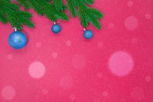 Spruce branches with blue Christmas tree shiny toys on pink background with snow bokeh. Copy space photo