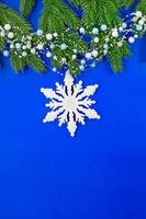 Christmas tree branches with garland of beads and snowflake on blue background. Christmas and New Year background. Vertical. Copy space photo