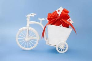 bicicleta con caja de sembradora con lazo rojo de guisantes de caja blanca sobre fondo azul. feriado, san valentín, día internacional de la mujer y la madre, 8 de marzo, cumpleaños. copie el espacio foto