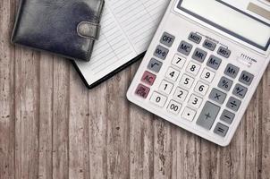 Office flat lay composition with calculator, address book and black purse on brown wooden table background with top view. Accountant paperwork concept photo