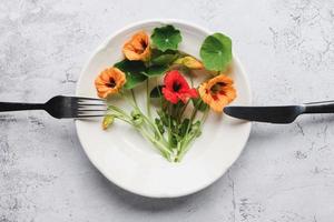 Nasturtium plants, Indian cress flowers and leaves in plate on kitchen table, top view photo