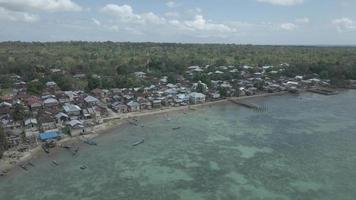 antenne visie van dorp in de buurt mooi strand met klein eiland in de achtergrond in maluku, Indonesië video