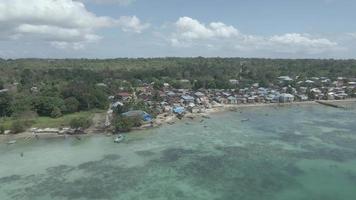 aereo Visualizza di villaggio vicino bellissimo spiaggia con piccolo isola nel il sfondo nel maluku, Indonesia video