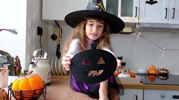 Child decorates the kitchen in home for Halloween. Girl in a witch costume plays with the decor for the holiday - bats, jack lantern, pumpkins. Autumn comfort in house, Scandi-style kitchen, loft video