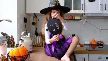 niño decora la cocina en casa para halloween. una chica disfrazada de bruja juega con la decoración de las vacaciones: murciélagos, farolillos, calabazas. comodidad otoñal en casa, cocina de estilo escandinavo, loft video