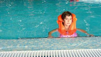 A child in an orange life jacket swims in the pool in an aqua complex for family holidays. Safety on the water, learning to swim video