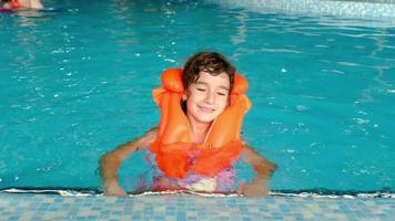 A child in an orange life jacket swims in the pool in an aqua complex for family holidays. Safety on the water, learning to swim video
