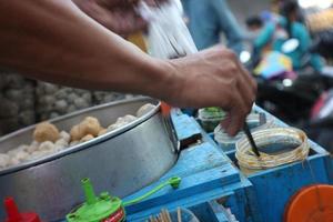 The seller of  meatballs, kojek is serving buyers using a cart on a motorbike around selling his wares. photo