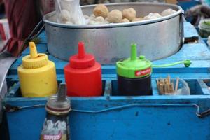 The seller of meatballs, kojek is serving buyers using a cart on a motorbike around selling his wares. photo